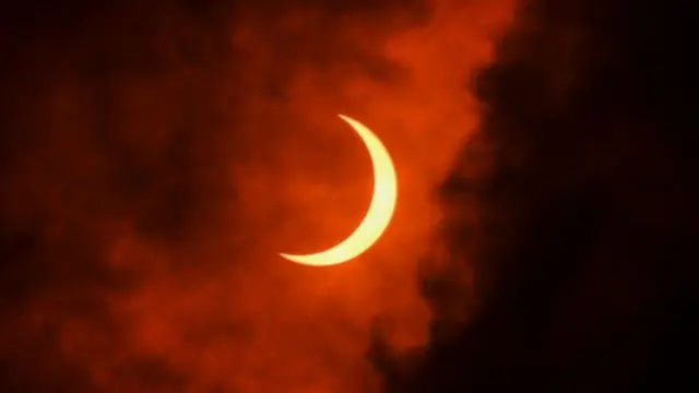 ดวงจันทร์กำลังเคลื่อนผ่านหน้าดวงอาทิตย์ในระหว่างเกิดสุริยุปราคา ผ่านม่านเมฆเหนือกรุงนิว เดลี ของอินเดีย