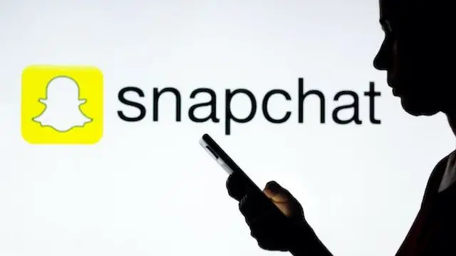La silhouette d'une femme tient un smartphone avec le logo Snapchat en arrière-plan.