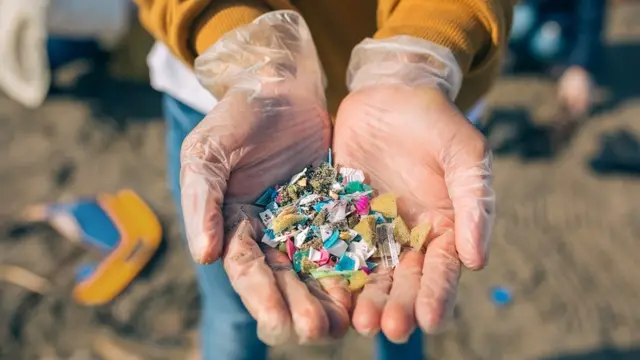 Detail of hands showing multi coloured microplastics on the beach