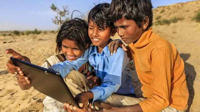 Crianças olham sorrindo para tablet na Índia