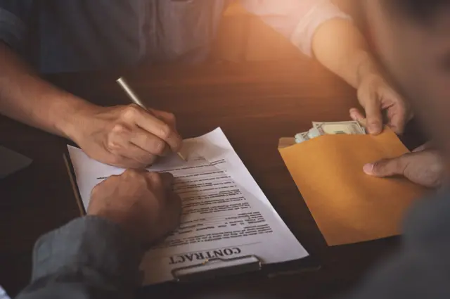 Un hombre firma un contrato a cambio de un sobre de dinero