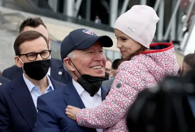President Joe Biden, flanked by Polish Prime MInister Mateusz Morawiecki, holds a child as he visits Ukrainian refugees at the PGE National Stadium, in Warsaw, Poland March 26, 2022