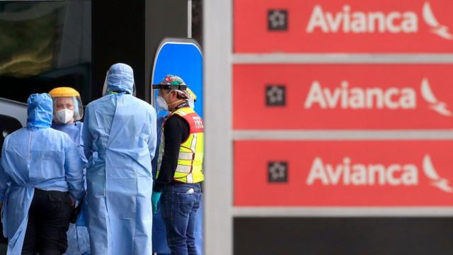 Un grupo de empleados con máscara al lado de un cartel de Avianca