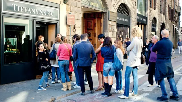 Un grupo de gente hace fila a la entrada de una tienda.