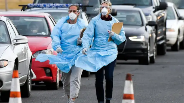 Personal médico andando al lado de una fila de autos.