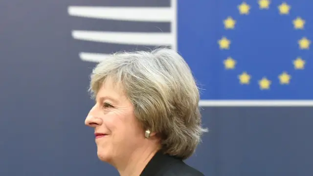 Theresa May com a bandeira da União Europeia ao fundo