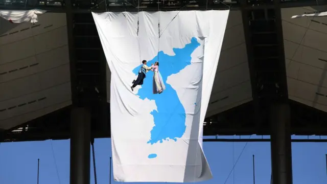 ศิลปินเกาหลีใต้ระหว่างการแสดงที่มีธงรวมชาติเกาหลีขนาดใหญ่เป็นฉากหลัง