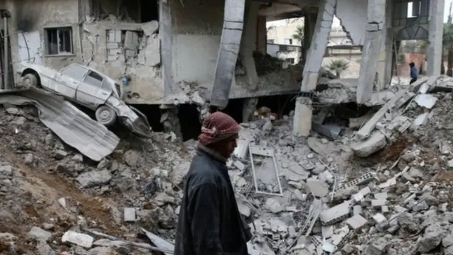 બોમ્બમારામાં ધરાશાયી થયેલી ઇમારતના કાટમાળની વચ્ચે પસાર થઈ રહેલો વ્યક્તિ