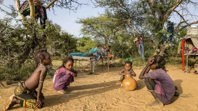Wasu yara na wasan kasa yayinda da iyayensu ke kwance Children play in the sand as their mother wakes up.