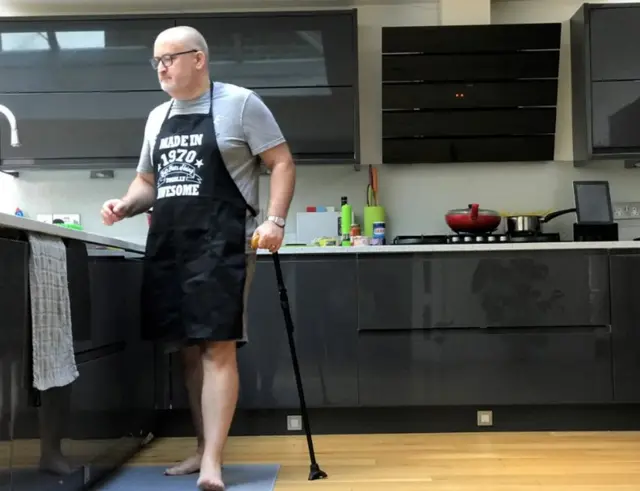 Ian Taverner standing in his kitchen with his walking stick