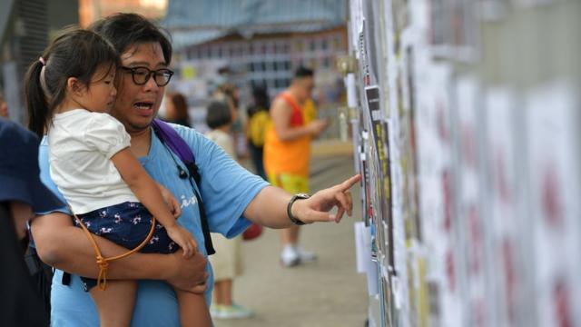 香港金钟“反送中”“连浓墙”示威现场一位男士向怀中女儿介绍墙上抗议宣传海报内容（28/9/2019）