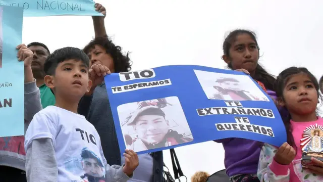 Duas crianças seguram um cartaz com fotos do tripulantes do Ara San Juan e os dizeres: 'tio, te esperamos, sentimosvbet ehs10falta'