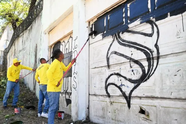 Reclusos del penal La Esperanza, escoltados por guardias, borran un grafiti vinculado a la pandilla Mara Salvatrucha durante un operativo que busca recuperar barrios controlados por pandillas en San Martín, El Salvador el 22 de marzo de 2023. - Hace un año, una ola de Los homicidios en El Salvador llevaron al presidente Nayib Bukeke a iniciar una "guerra" contra las pandillas que ha llevado a más de 65.000 personas a prisión. Su acción devolvió la tranquilidad a la población, pero le ha valido críticas de organismos de derechos humanos.