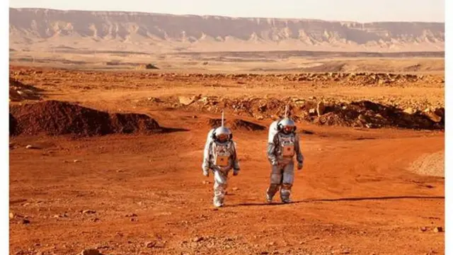 Dois homens com roupas prateadasroleta de números de 1 a 20astronautas andamroleta de números de 1 a 20um deserto laranja que lembra a superfícieroleta de números de 1 a 20Marte