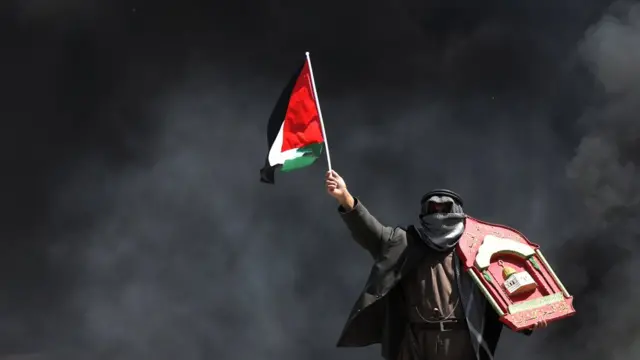 Un manifestante palestino ondea una bandera en medio del humo