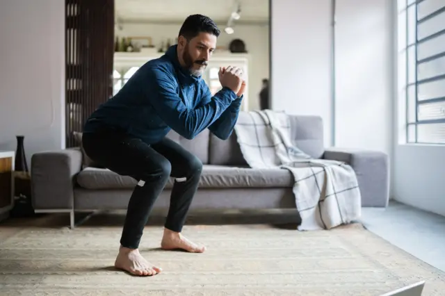 Un hombre hace sentadillas en la sala de su casa.