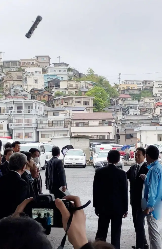 Thời điểm quả bom khói bay về phía Thủ tướng Kishida, người đứng quay lưng lại hướng bom ném tới.