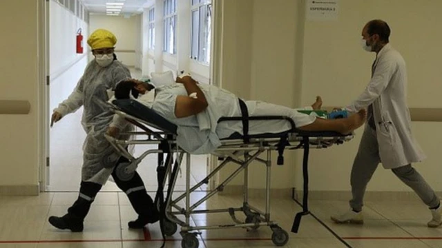 Profissionais de saúde carregam paciente em maca