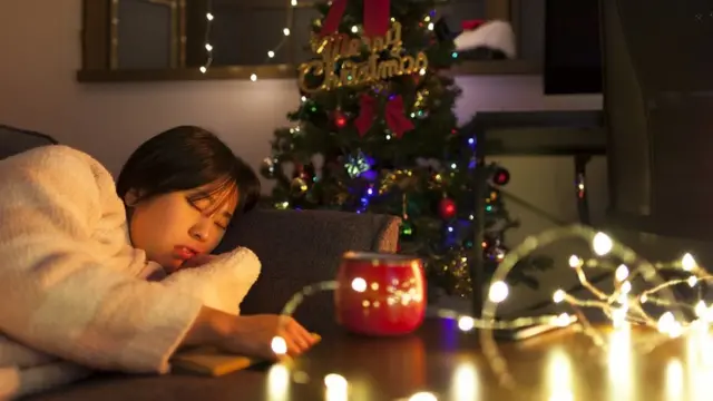 Young woman dozing on the sofa, Christmas tree in the background and Christmas lights in the foreground