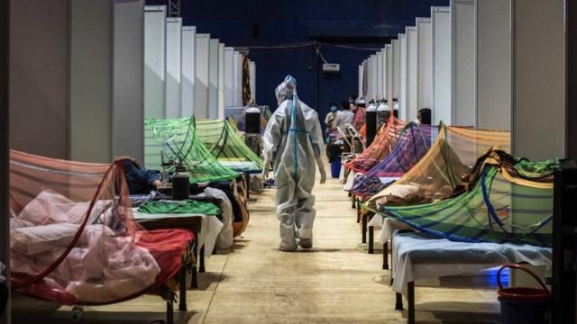 新德里英联邦运动会村体育场内的临时护理设施内，一名身穿个人防护装备的医务人员正在观察感染新冠的患者（2021年5月2日）