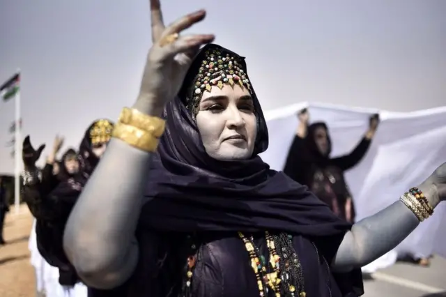 Sahrawi women perform a dance in the parade. Their faces are painted white.