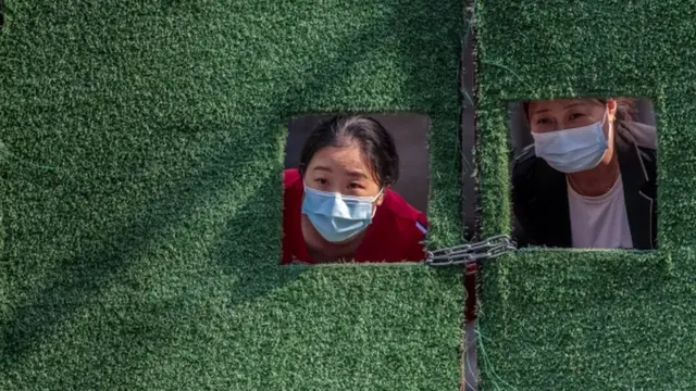 Women in quarantine look through small windows in a green fence, amid the Covid-19 lockdown in Shanghai, on 2 May 2022