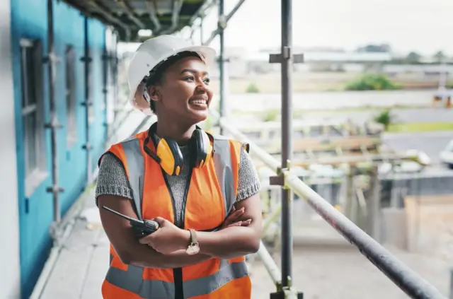 Foto colorida mostra trabalhadora negra com uniformejogo de ganhar dinheiro casinouma construção, sorrindo