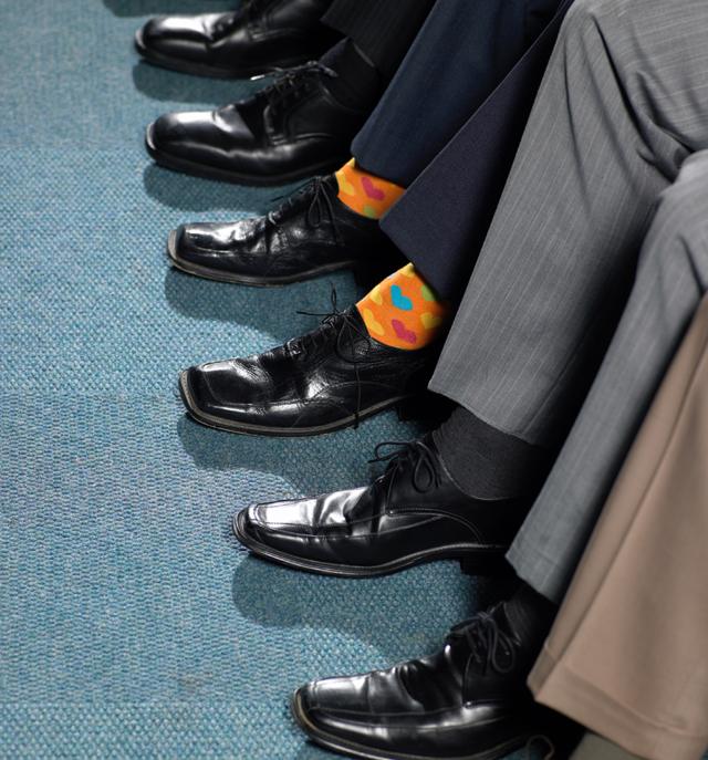 Un hombre con medias naranjas, entre pies con medias oscuras