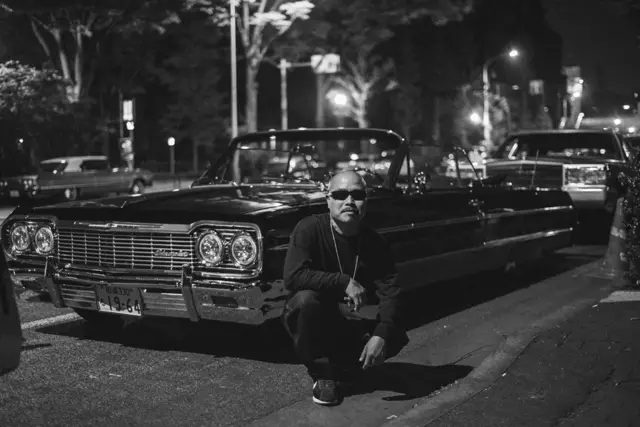 Chicano japonés frente a su auto "lowrider"
