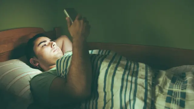 బెడ్ మీద పడుకుని ఫోన్ చూస్తున్న యువకుడు