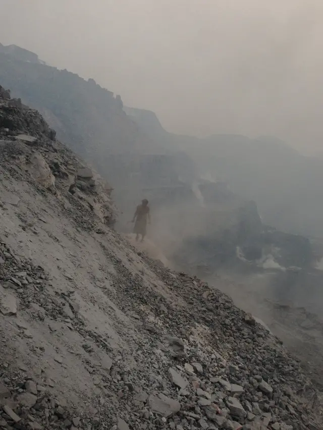 Un hombre camina sobre una montaña de carbón y ceniza.