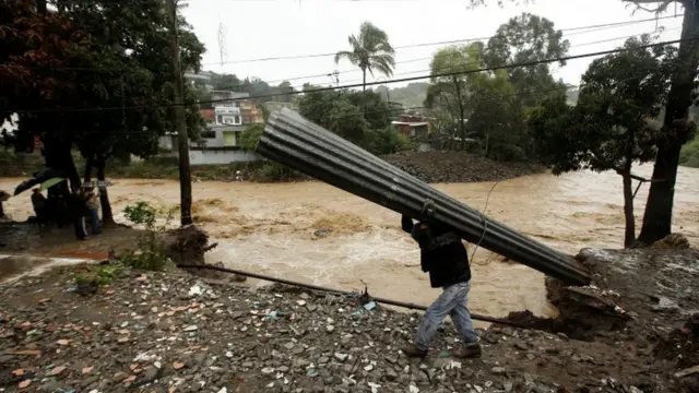 Homem recupera folhasbetsulzinco, após deslizamento destruir casas na Costa Rica.