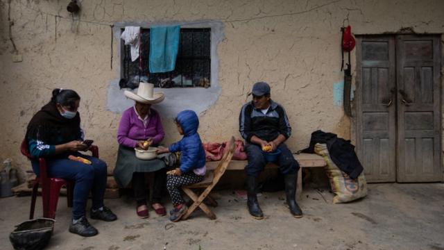 Una familia en Cajamarca está a las afueras de una casa rústica desgranando maíz.
