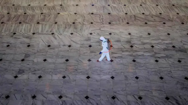 Seorang petugas kesehatan mengenakan alat pelindung diri menyemprotkan disinfektan pada lantai sebuah gedung.