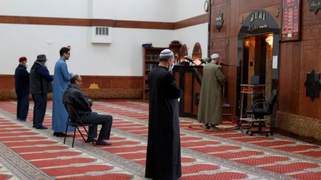 Imam Magdy Badr na jan sallar Jam'i kai tsaye ta na'urarsa kusan masallacin babu kowa, Masallacin Al-Salaam da ke birnin Dearborn a Michigan, saboda tabbatar da tazara tsakanin mutane ana yin sallar a warware a irin matakan da duniya ke dauka da kuacewa annobar corona. An dauki hoton ne a ranar 24 ga watan Afrilun 2020.