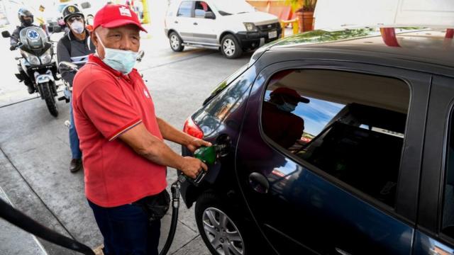 Un empleado de una estación de gasolina llena el tanque de un auto.