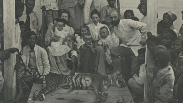 Para pemburu - melibatkan penjajah Belanda dan warga lokal- menunjukkan seekor harimau di depan rumah di Indonesia.