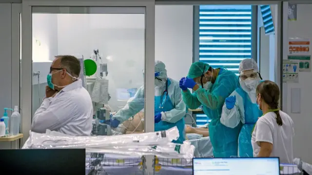 Médicos com equipamentos de proteção atendem paciente, cujo rosto não é visível, em cama de hospital na espanha