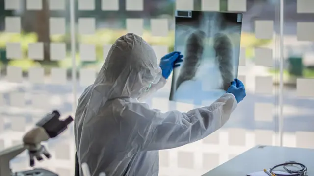 Un médico protegido con un traje observa una radiografía