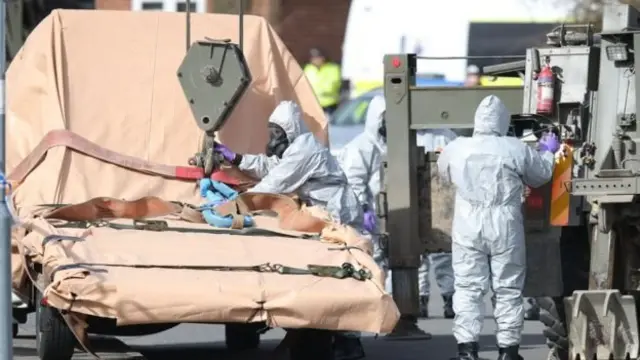 Soldiers wearing protective clothing prepare to lift and recover a vehicle in Gillingham, Dorset