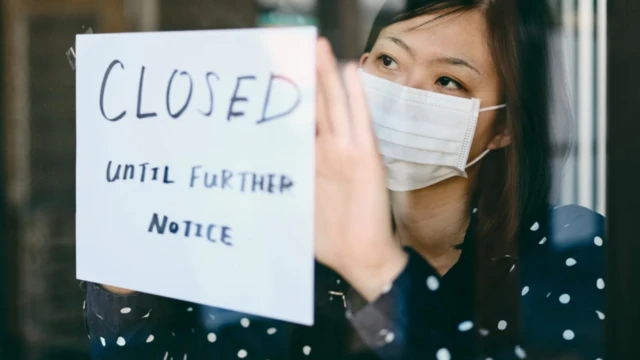 Une femme colle un panneau "fermé jusqu'à nouvel ordre" sur une porte.