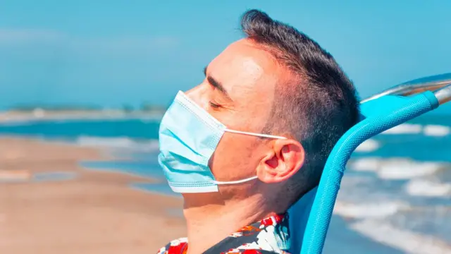 رجل يرتدي كمامة ويجلس على شاطيء