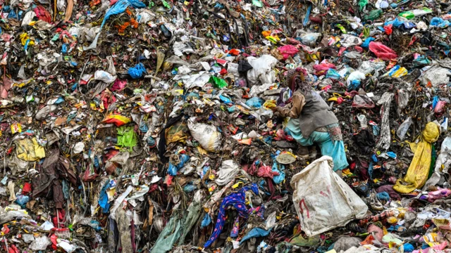 Una mujer casi no puede distinguirse entre la basura de un vertedero. Sus ropas son del mismo color que los residuos.