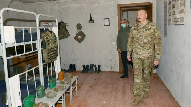 Алиев внутри комнаты декорированной как военная казарма.