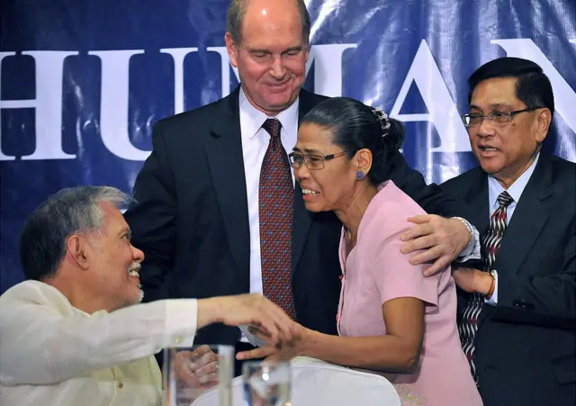 ক্ষতিগ্রস্ত একজন ফিলিপিনো নারীর হাতে ক্ষতিপূরণের চেক তুলে দিচ্ছেন ফিলিপিনের একজন আইনজীবী- পেছনে দাঁড়িয়ে রবার্ট সুইফট- ফেব্রুয়ারি ২০১১