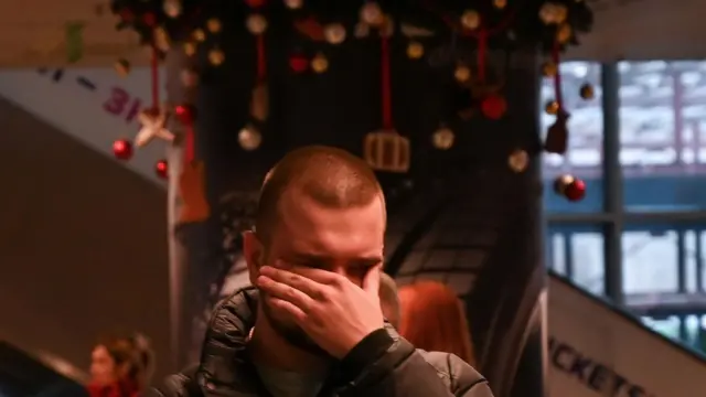 Молодой человек закрыл лицо рукой на фоне праздничной елки