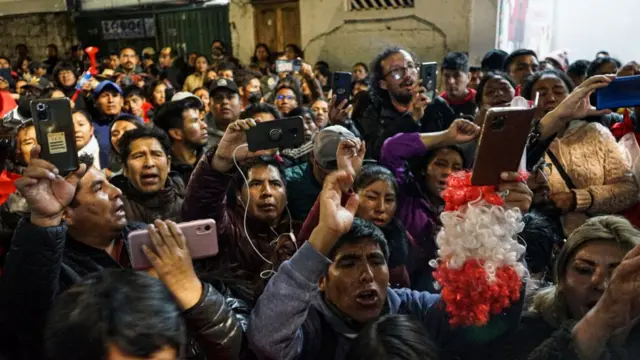 Manifestantes agrupados em uma sala; alguns filmam com celulares