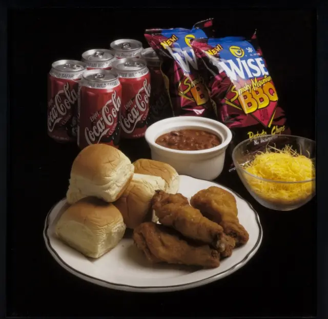 Uma refeição com frango, pãezinhos, feijão, batatas fritas e refrigerante