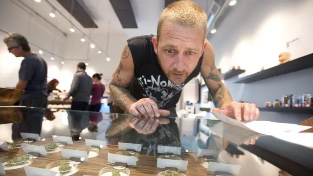 Hombre viendo en un escaparate en Oregón qué tipo de marihuana se va a comprar.