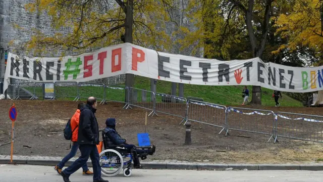 Personas caminan delante de una pancarta de protesta colgada cerca del Parlamento de Valonia.